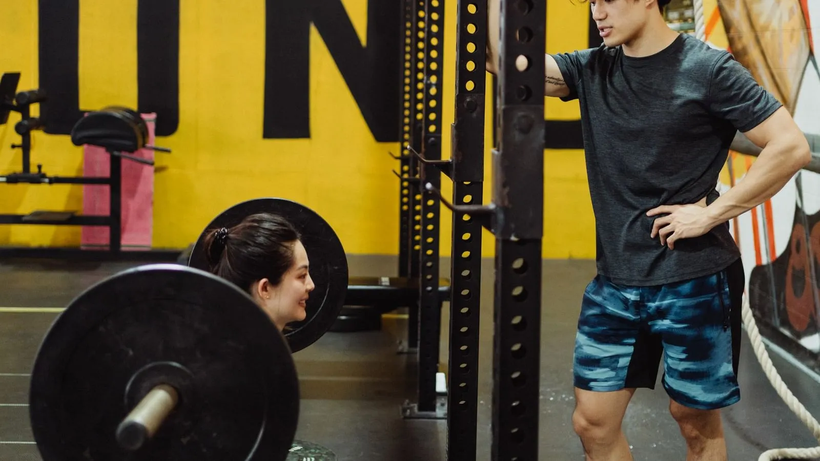 Woman squatting under a loaded barbell while a coach watches