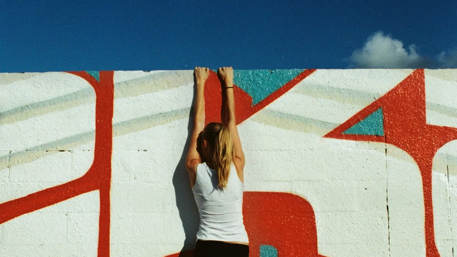 Woman hanging by her hands from the top of a painted wall
