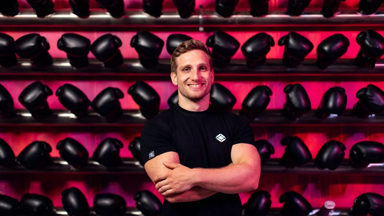 Smiling man with his arms crossed in front of a wall of kettlebells