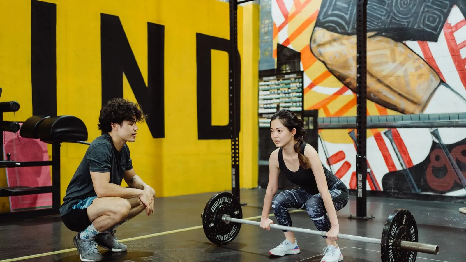 Coach crouching beside a woman lifting a barbell